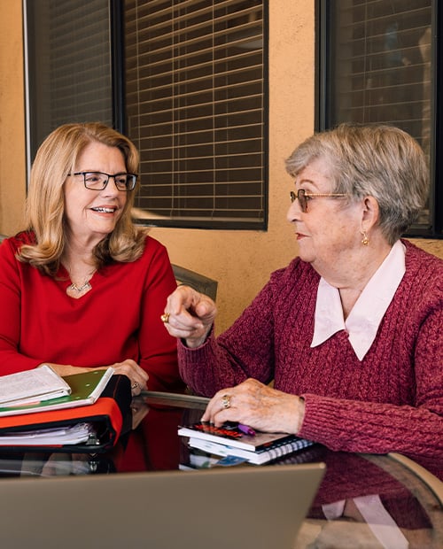 Two senior women with notebooks sit around a table during a writers' group meeting at Plymouth Village