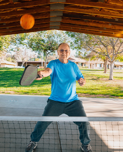 Senior man playing pickleball on the court at Plymouth Village