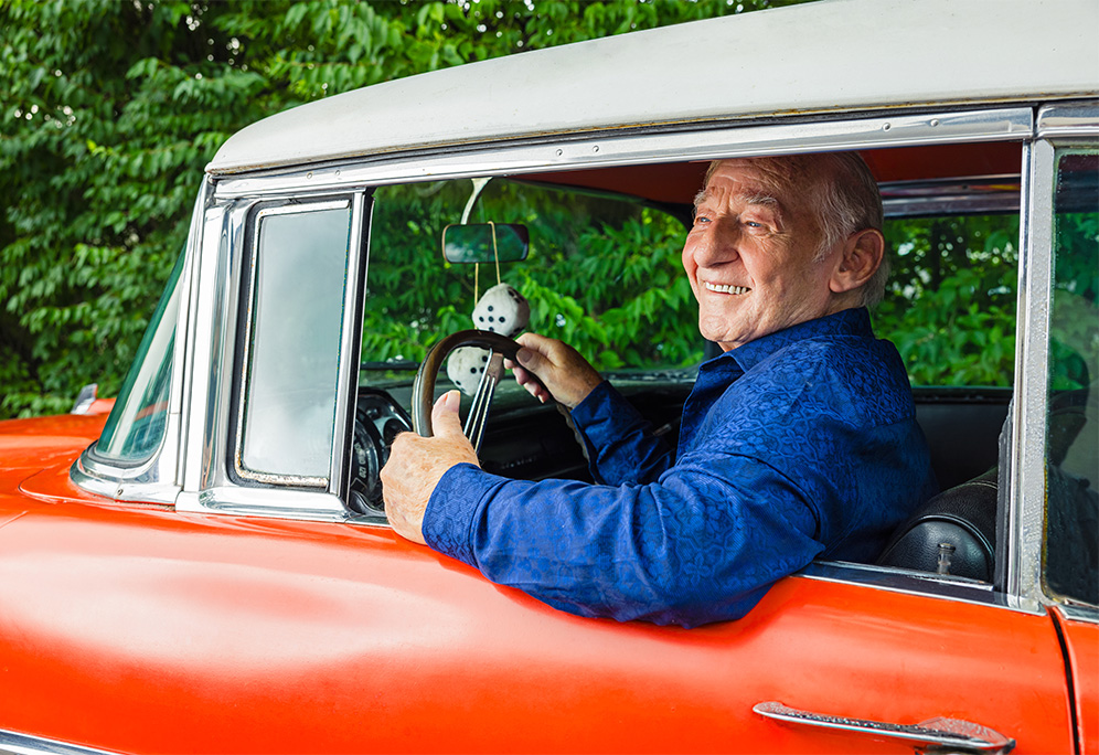 senior driving a red vintage car