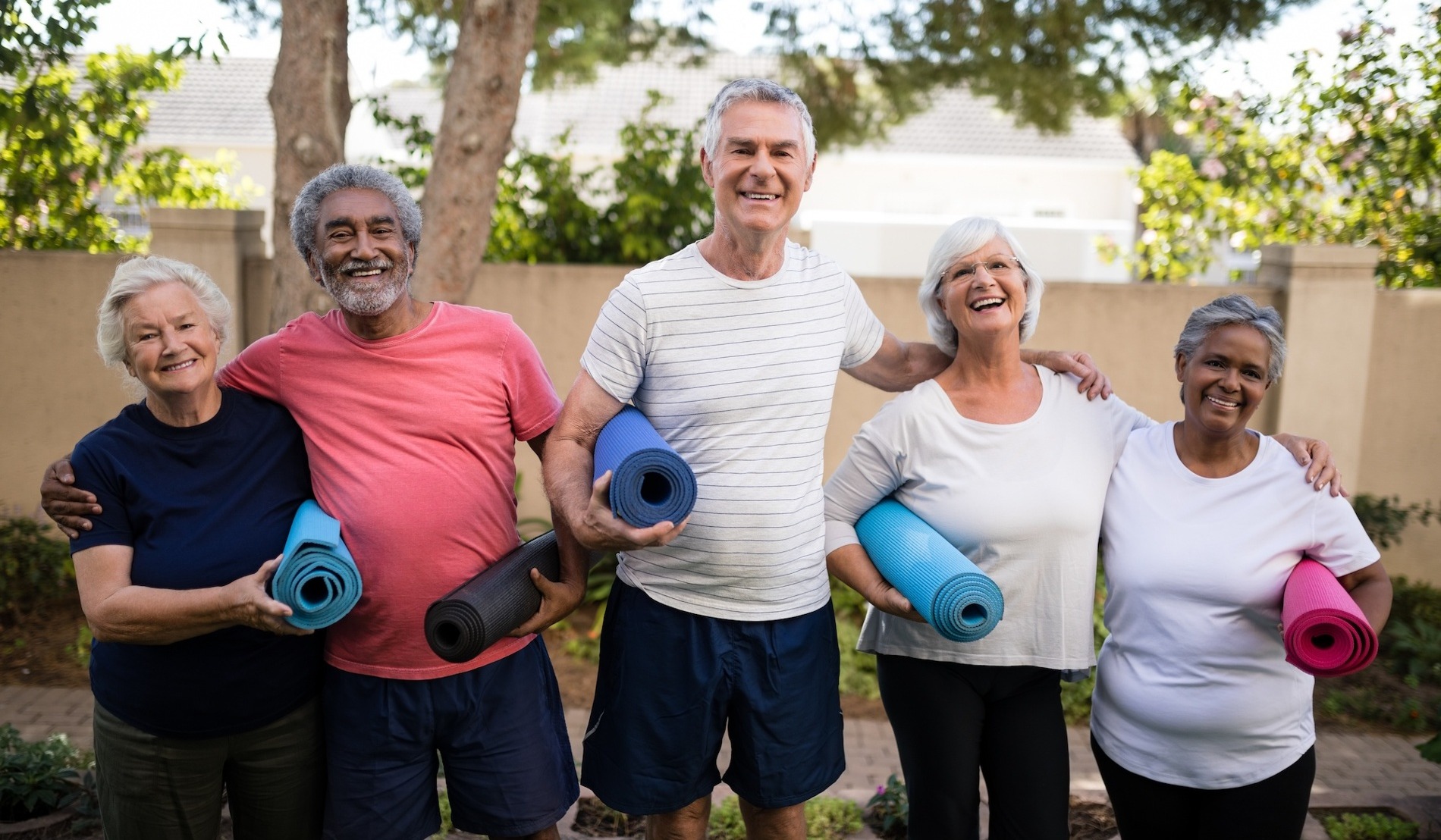 Group of smiling friends holding yoga mats outside