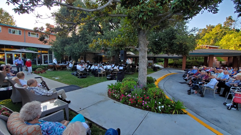 People seated in chairs outside watching a concert band.