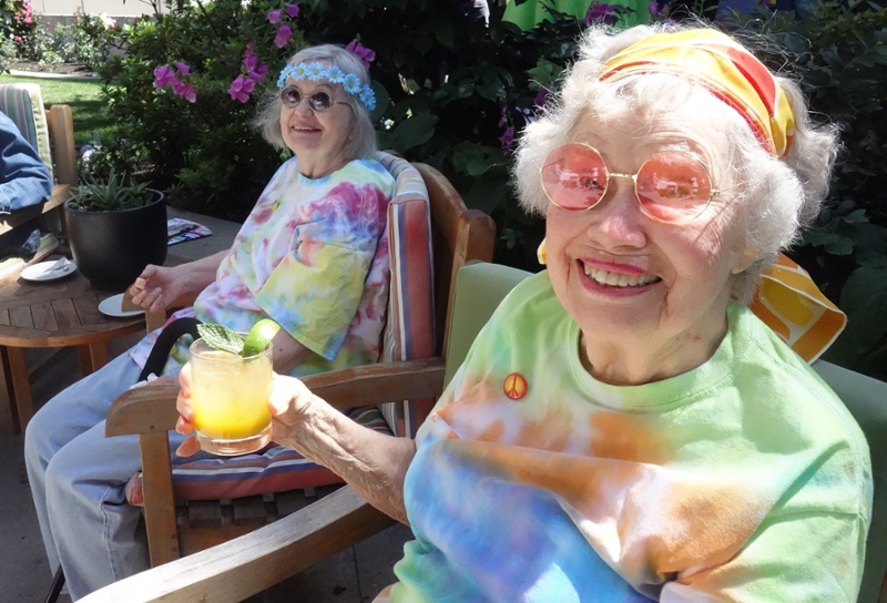 Two women wearing tie-dye hold up a cocktail.