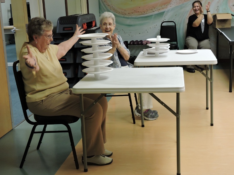 A senior resident with a tall tower that she constructed of plates and cups.