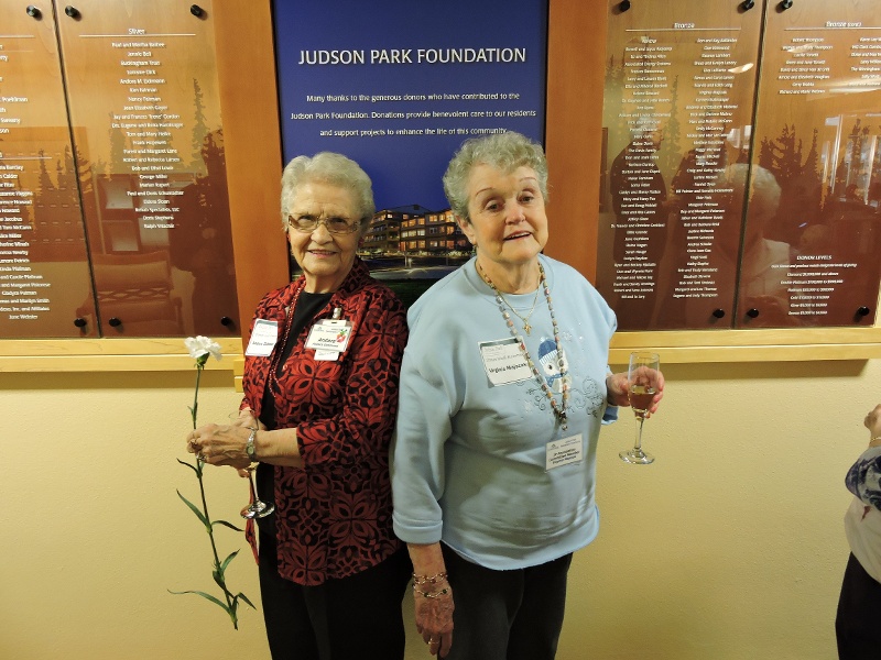 Two women holding a flower and champagne glass at a Judson Park Foundation event.