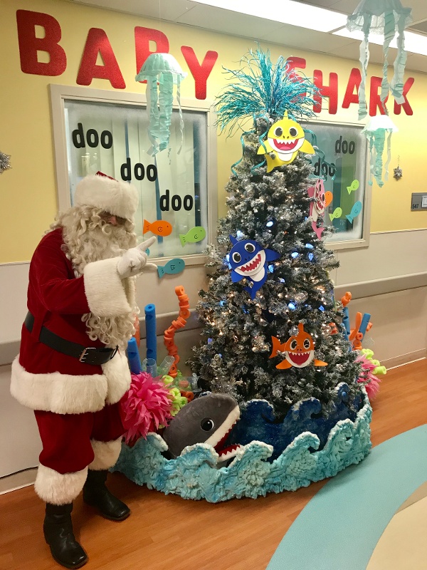 Resident dressed as Santa pointing to a Christmas tree.