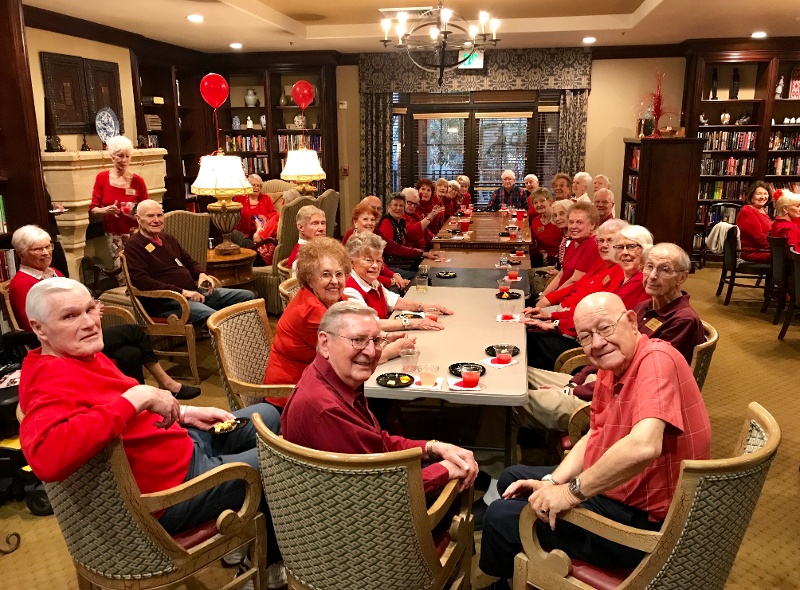 A group of seniors wearing red, sitting around a table.