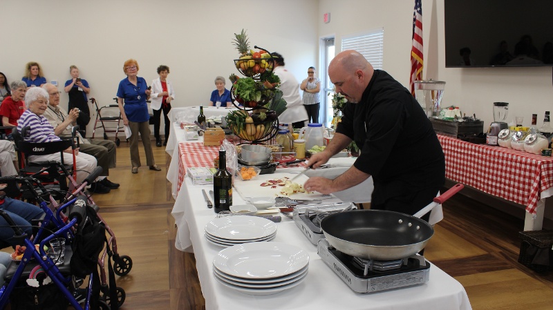 Chef chopping on a cutting board while and audience looks on.