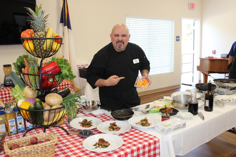 A chef pointing at an orange food in a bowl and frowning.