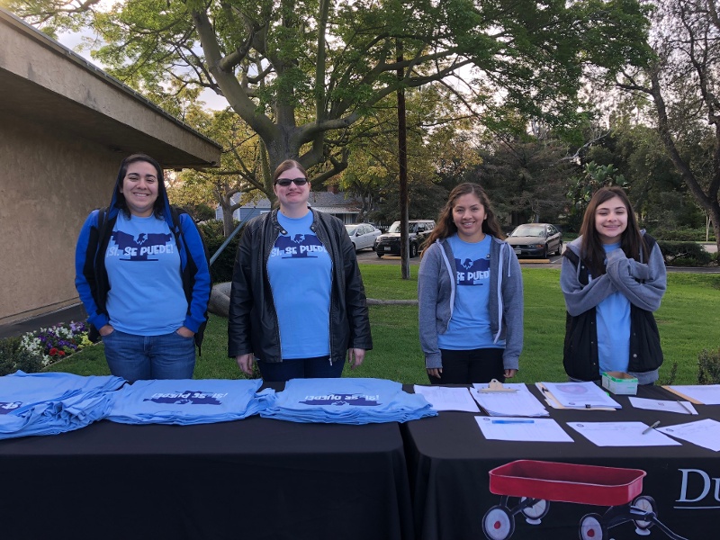 Four people standing behind a table with piles of blue t-shirts.