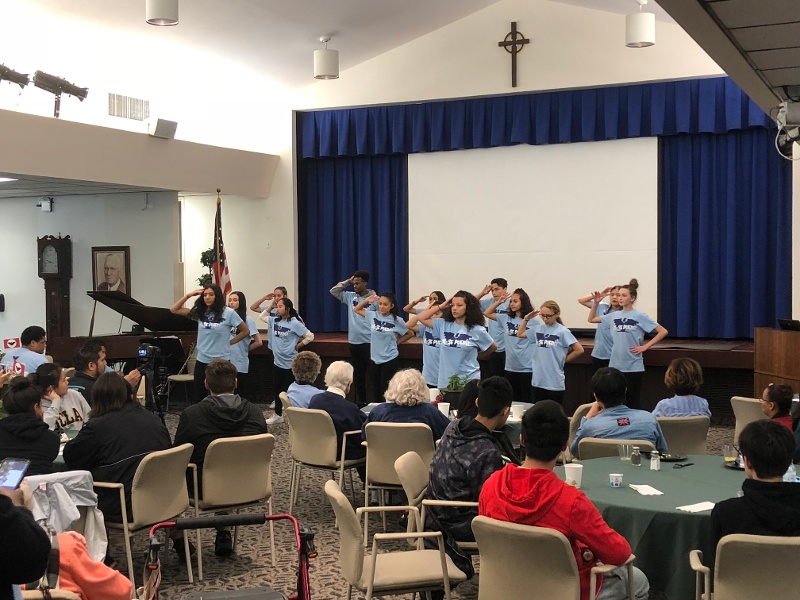 A group of girls in blue t-shirts saluting an audience.