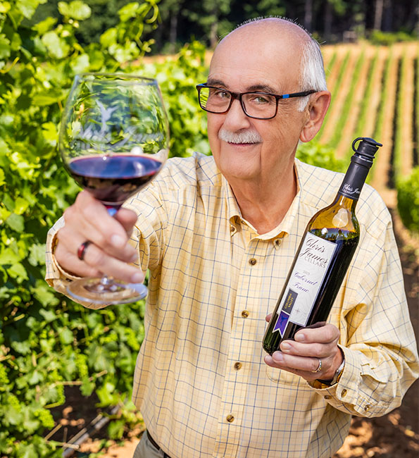 Rod in a vineyard holding up a glass and bottle of wine