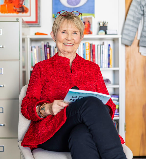 Sara sitting in office chair smiling while holding a book