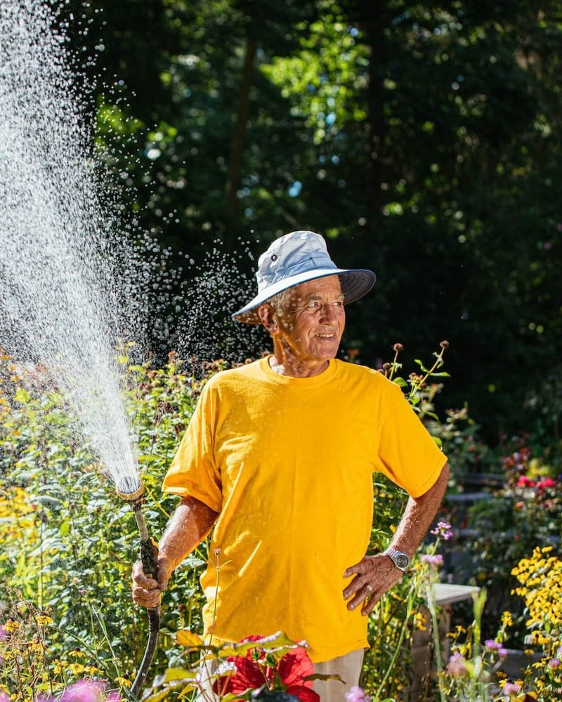 Man watering plants wearing a hat and yellow shirt