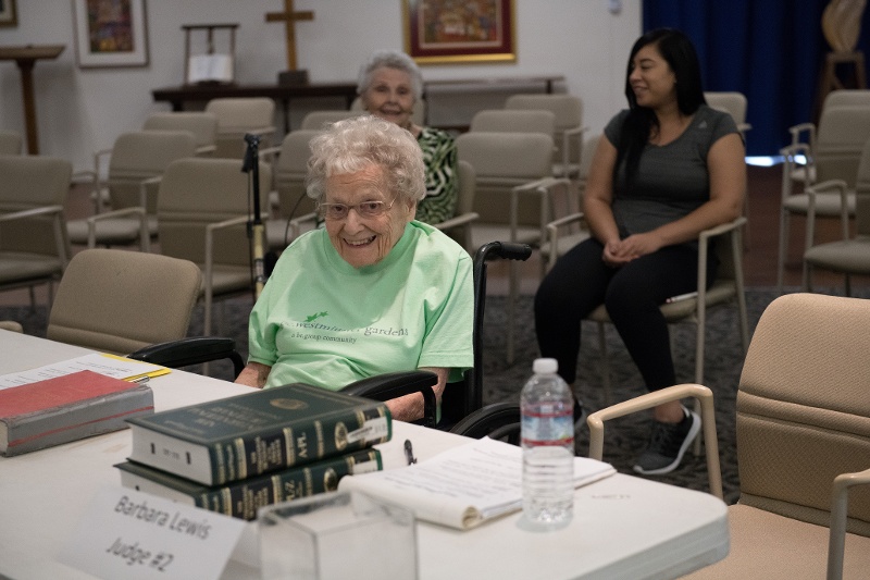 A smiling woman behind a table with dictionaries and a sign that reads 