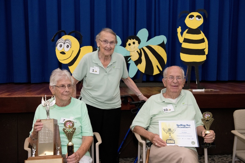 Spelling bee participants holding trophies and certificates.