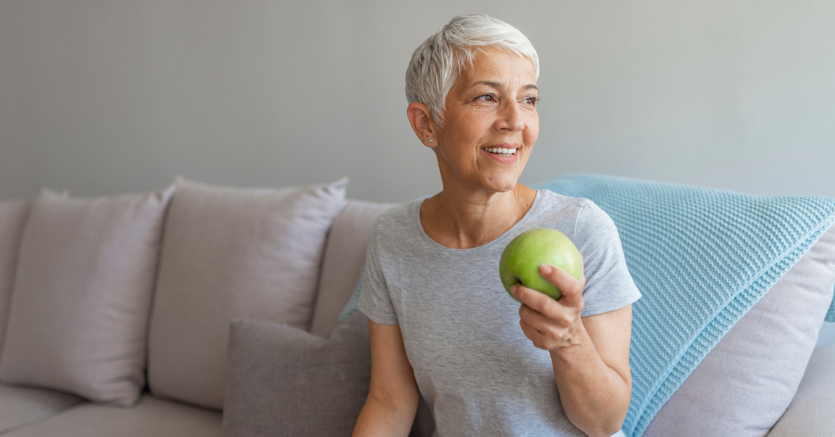 Woman sitting on couch smiling and eating an apple