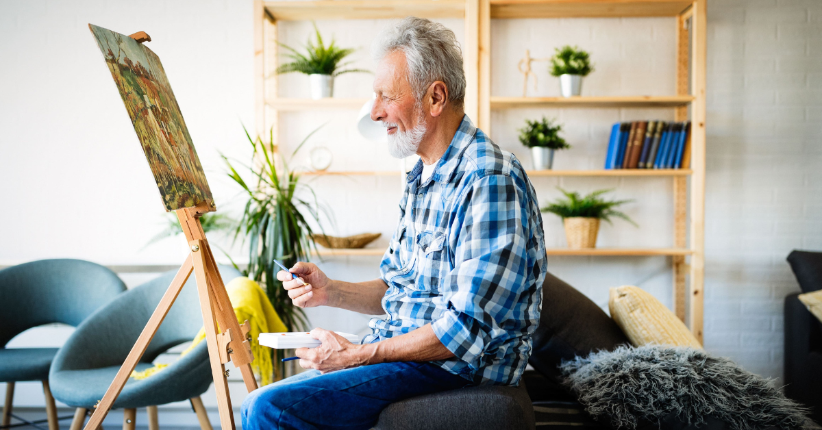 older man smiling and painting indoors