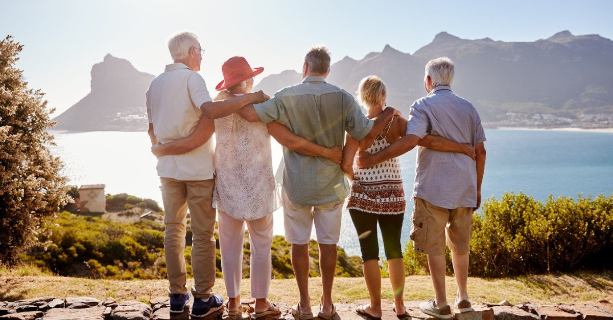 group of senior friends standing on a rock ledge and admiring the mountain views while wrapping their arms around each other