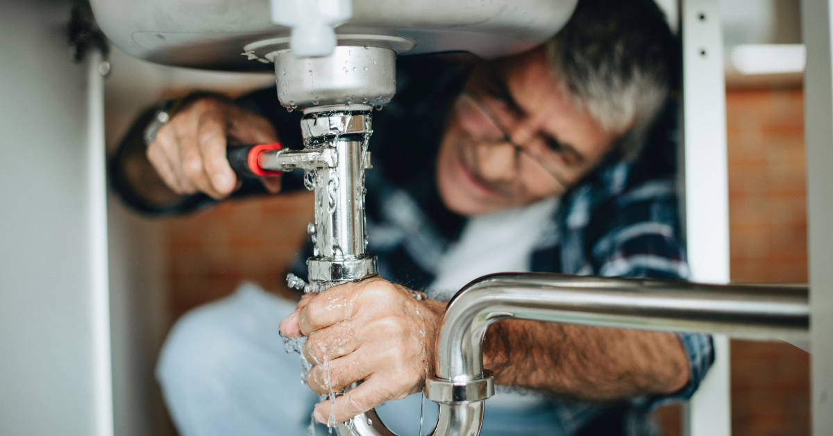 older man fixing leaky pipe under sink