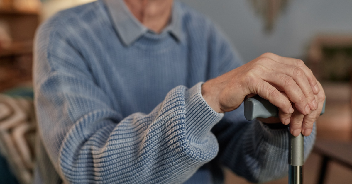 elderly man in a blue sweater leaning on his cane while he sits on the couch