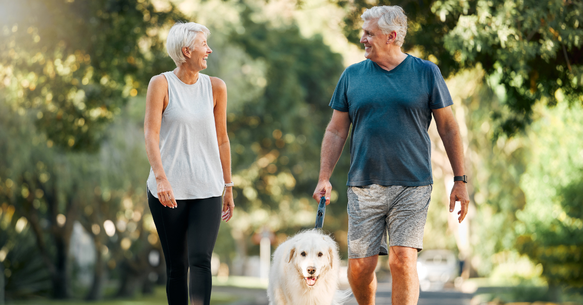 man and woman smiling and walking dog outside