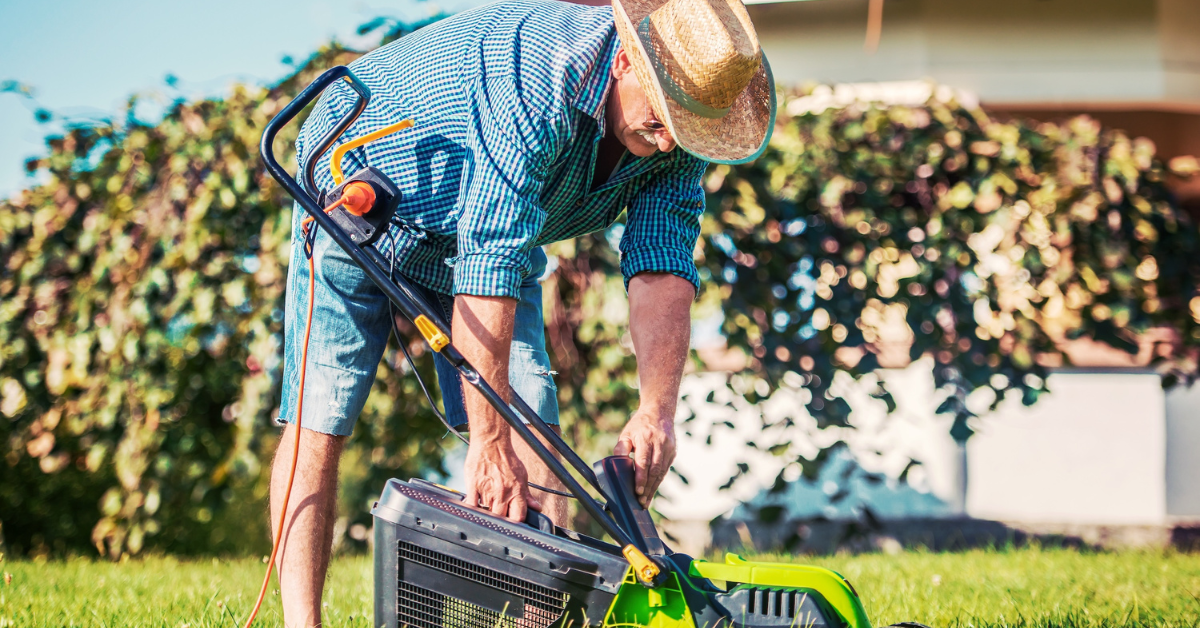 older man bending down to fix his lawnmower outside