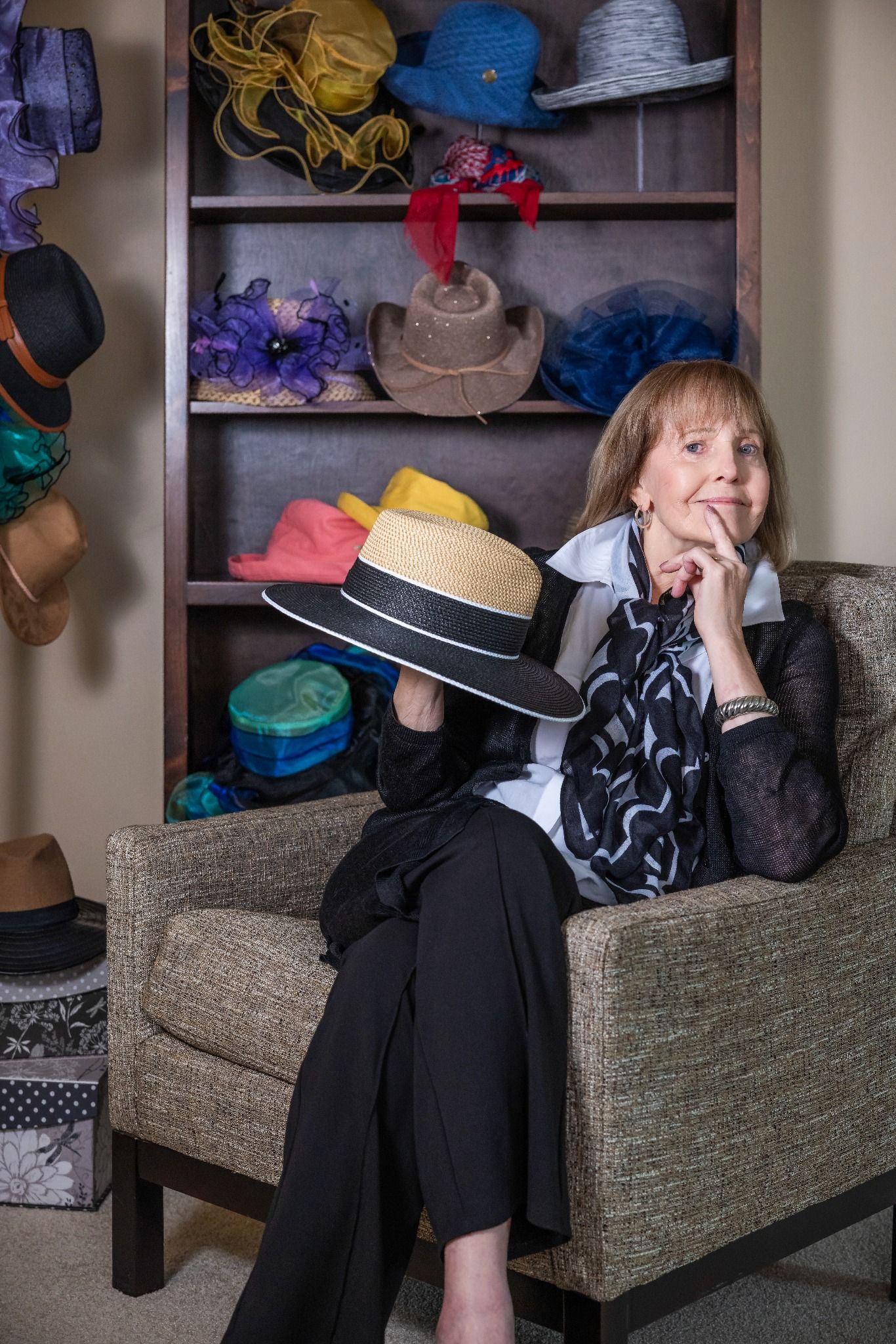 Linda sitting with a hat in front of her colorful hat collection.