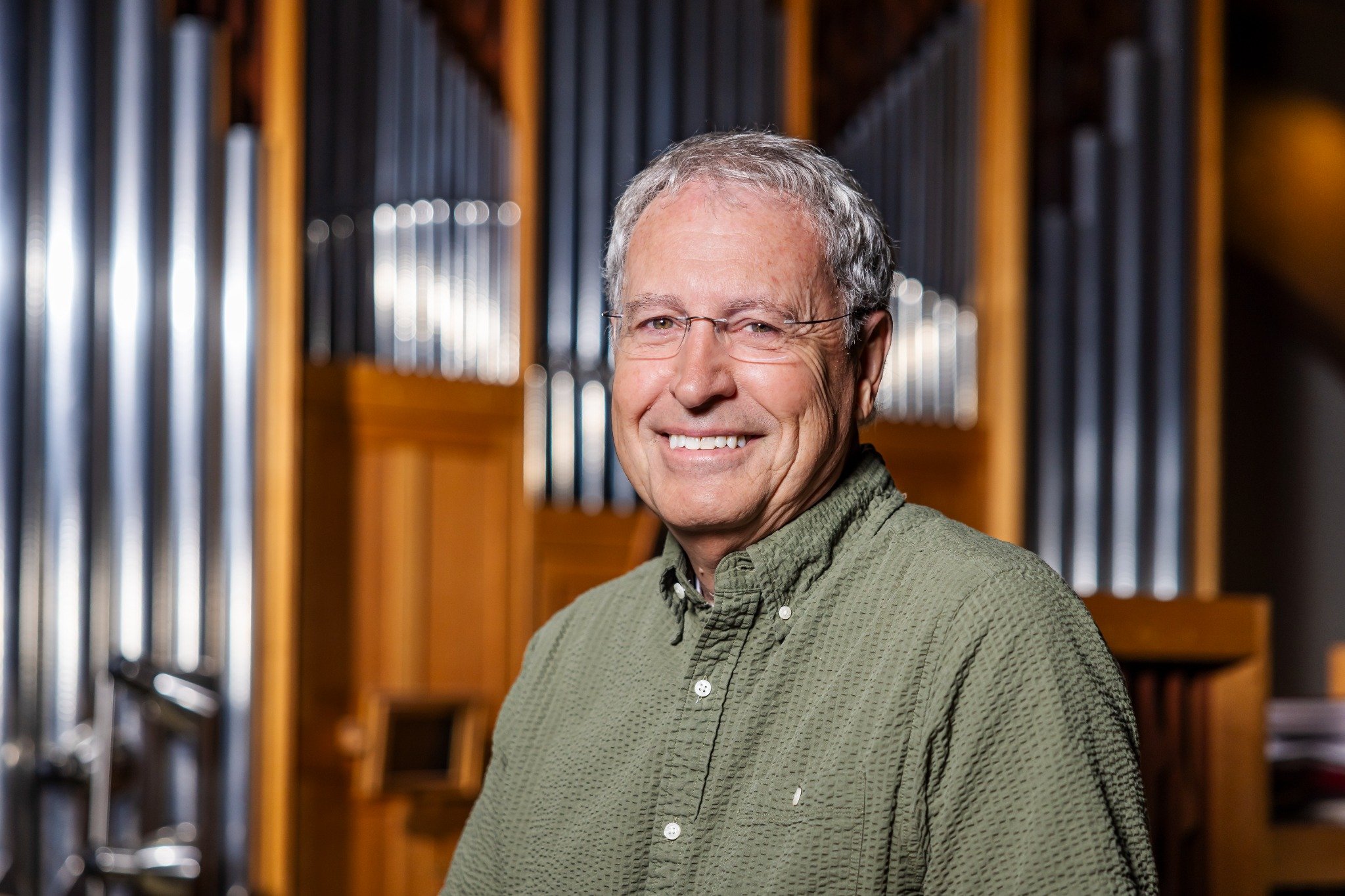 ohn smiling in front of church organ pipes.