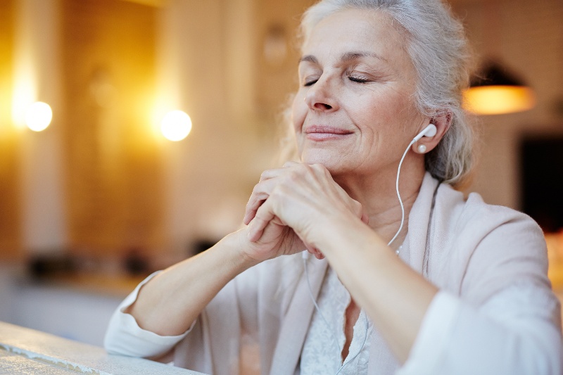 A woman with her eyes closed and wearing earbuds. 