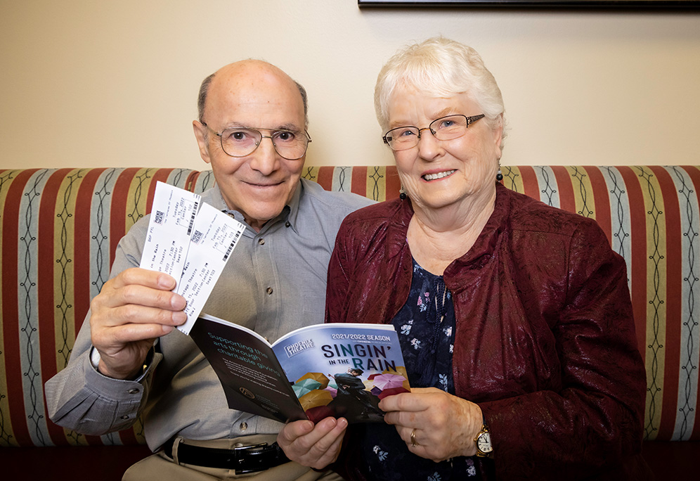 Joe and Diana holding up tickets to a play and a playbill to Singing in the Rain