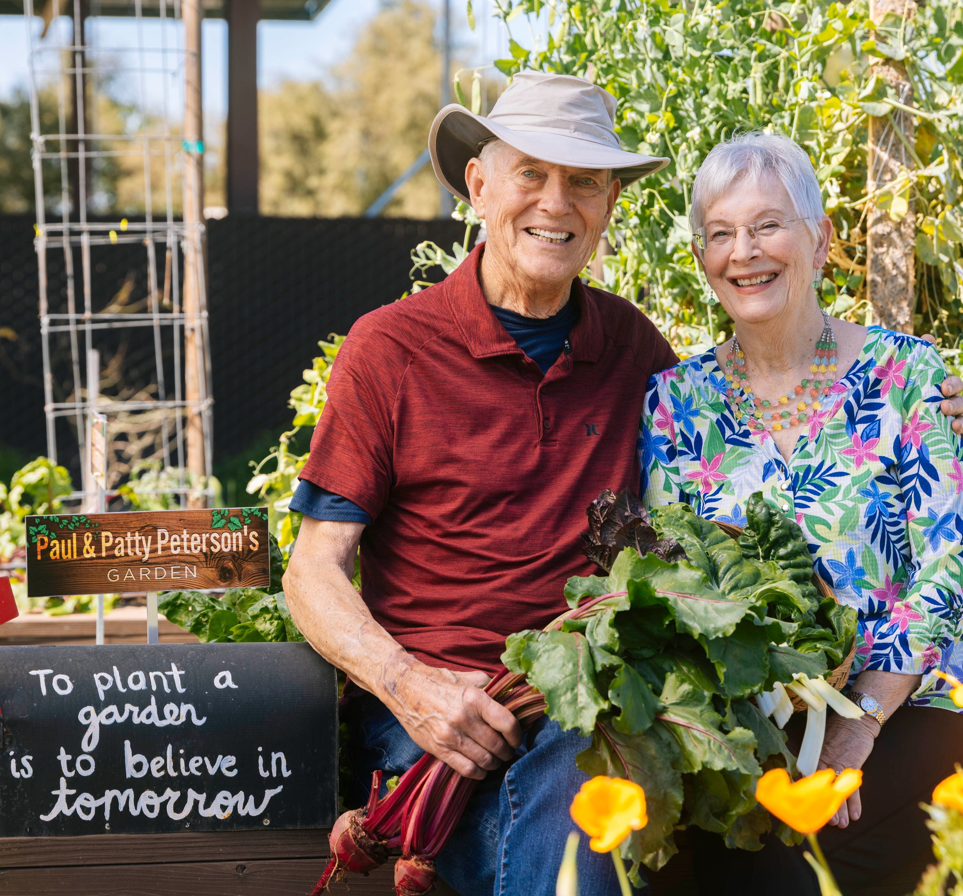Paul and Patty are sitting in a garden holding freshly pulled vegetables.