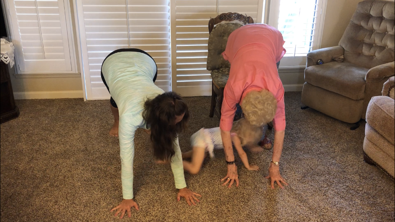 Mom and grandma doing downward dog while a baby crawls under them.